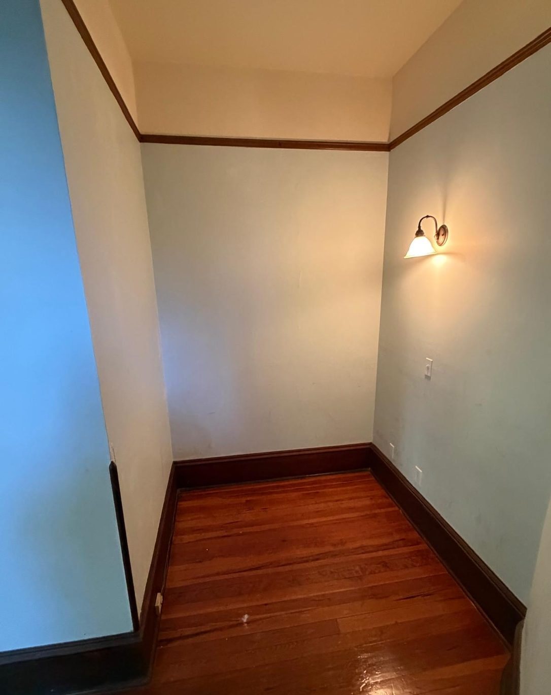 Today: an empty upstairs alcove with pale blue walls, dark stained baseboards, wood floors and a wall sconce.